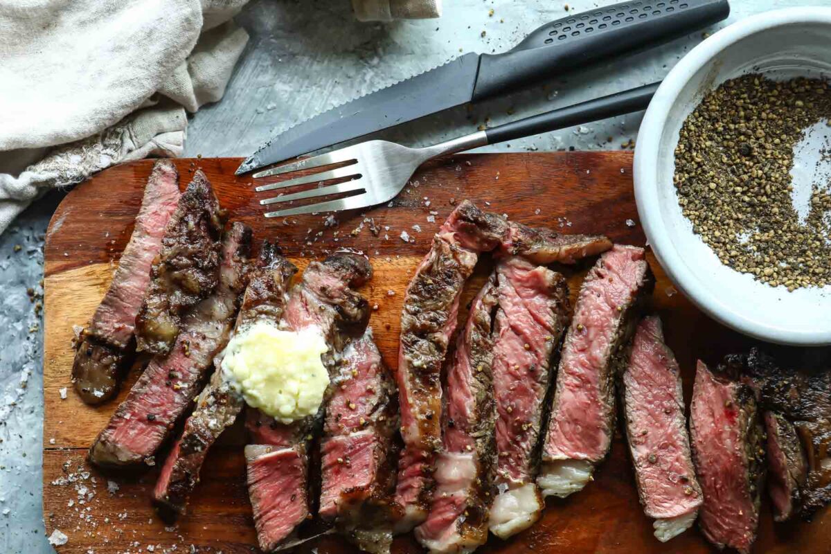 A sliced grilled ribeye on a wooden cutting board with a fork and knife.