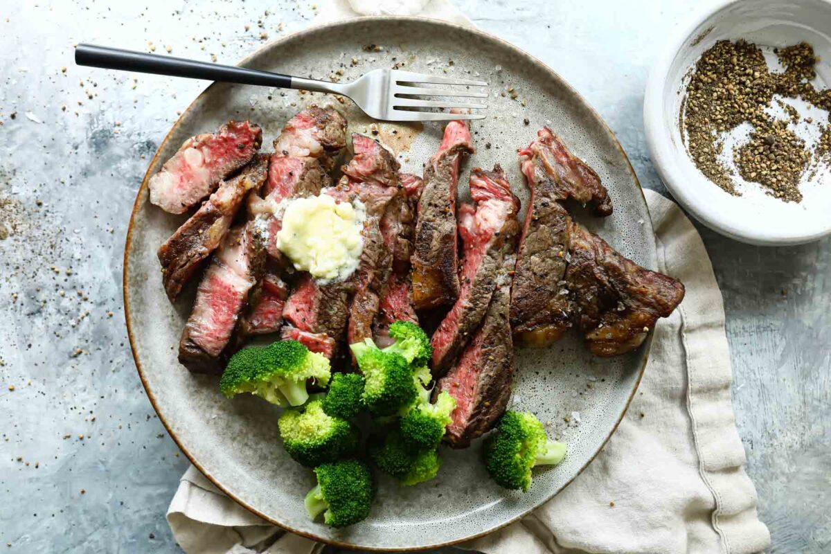 A grilled ribeye sliced on a plate served with broccoli.