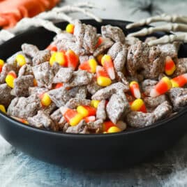 A bowl of Halloween puppy chow with two plastic skeletal hands reaching into it.