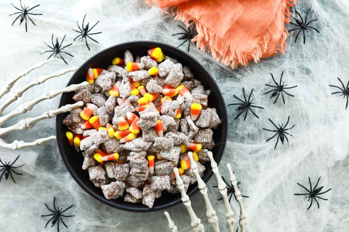 A bowl of Halloween puppy chow with two plastic skeletal hands reaching into it.