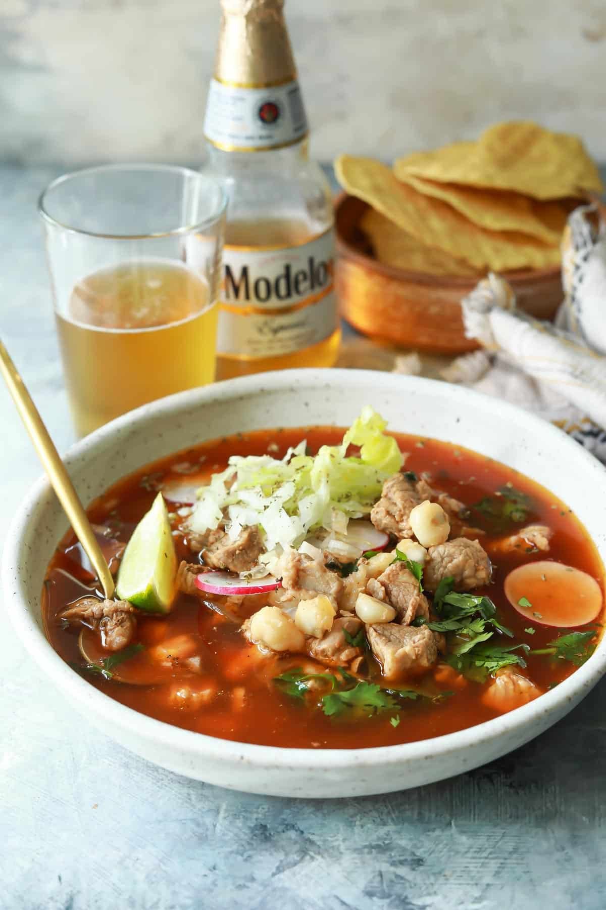 A bowl of pozole rojo with a Modelo behind it.