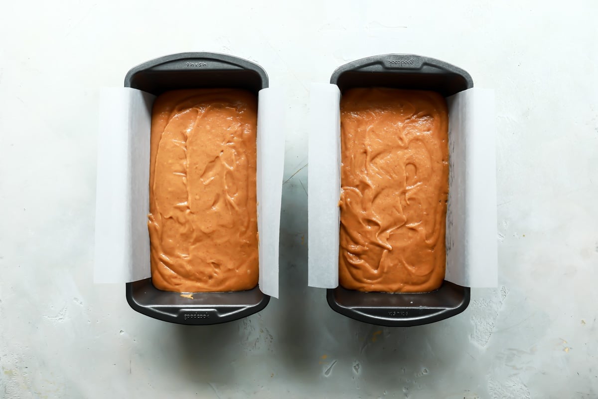 Two loaf pans with pumpkin bread batter in them.