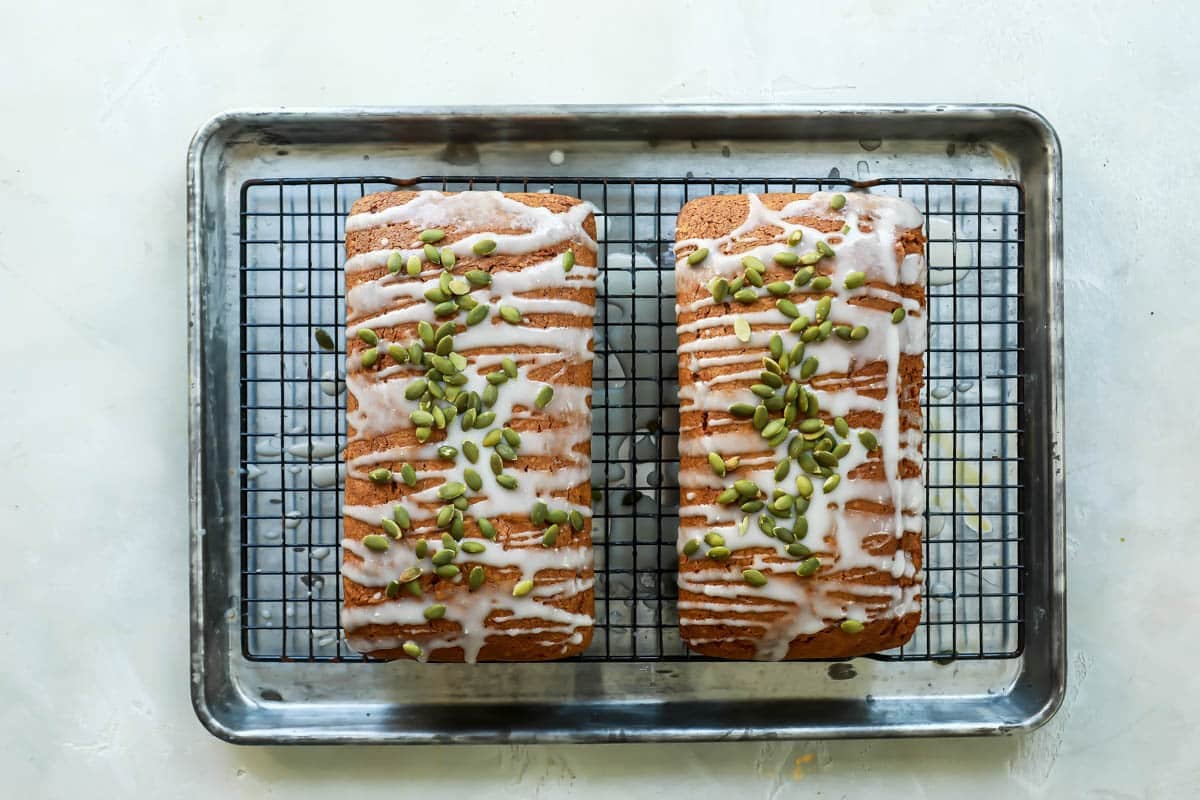 Two loaves of pumpkin bread after being topped with icing and pepitas.