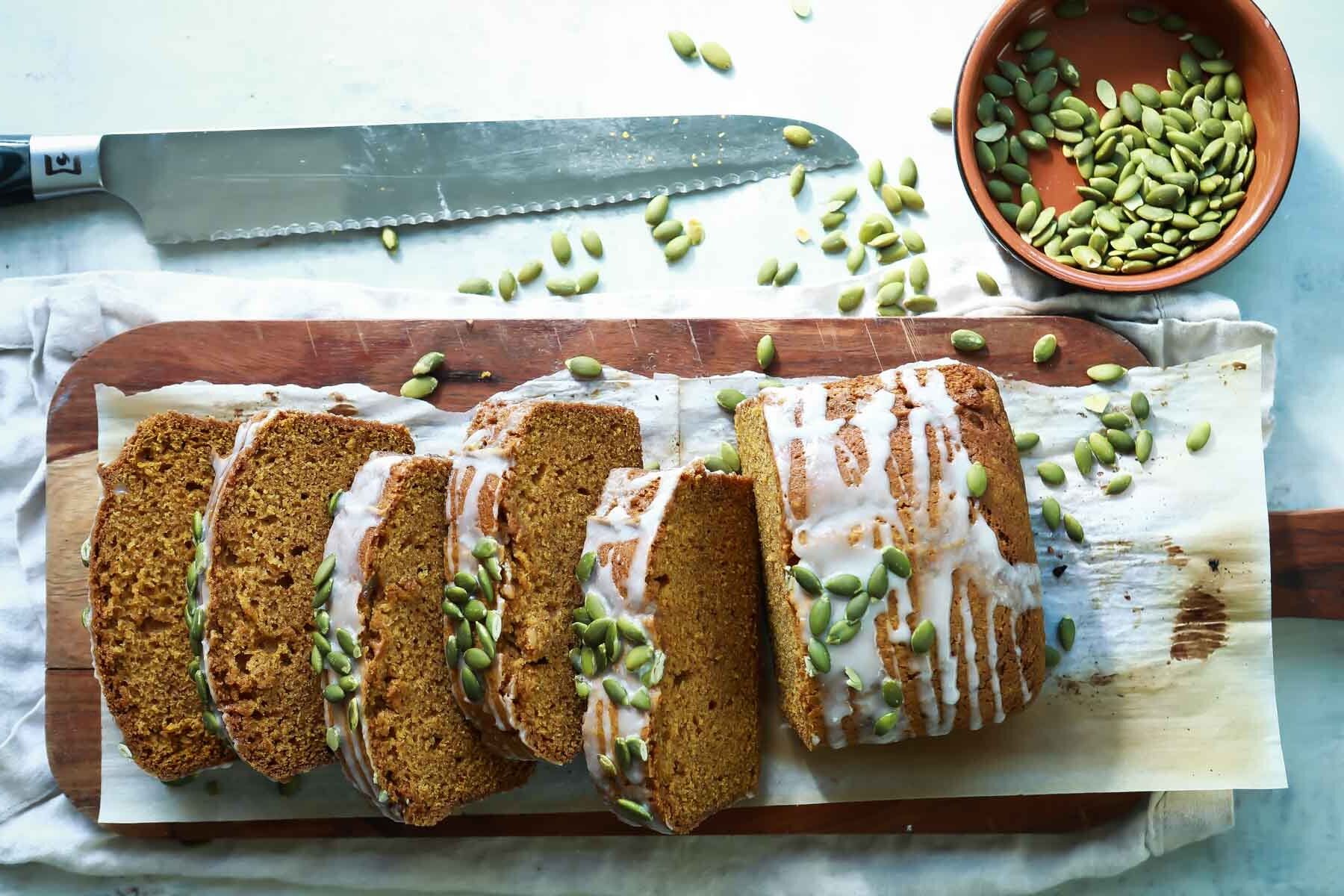 A loaf of pumpkin bread sliced on a wooden cutting board.
