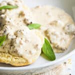 A white bowl of biscuits smothered in sausage gravy garnished with sage leaves.