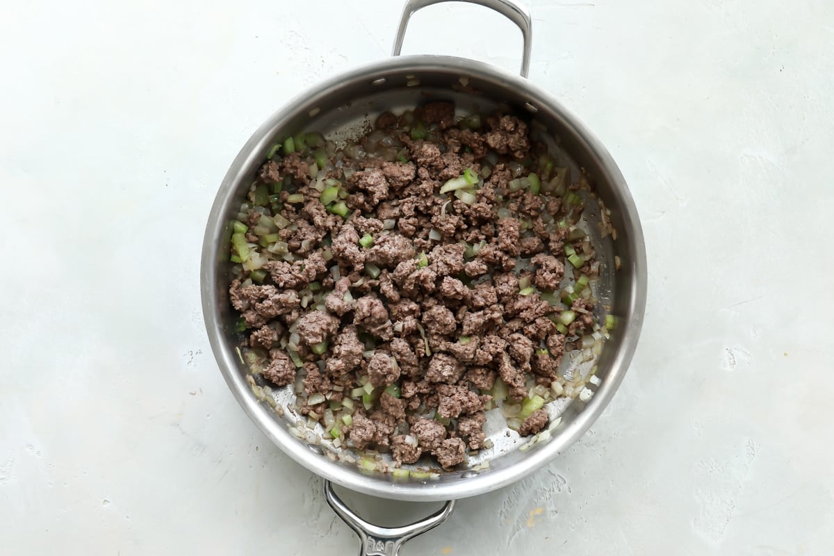 Beef, onions and celery being cooked in a silver skillet.