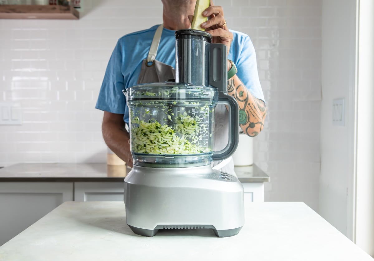 Someone using a food processor to grate zucchini.