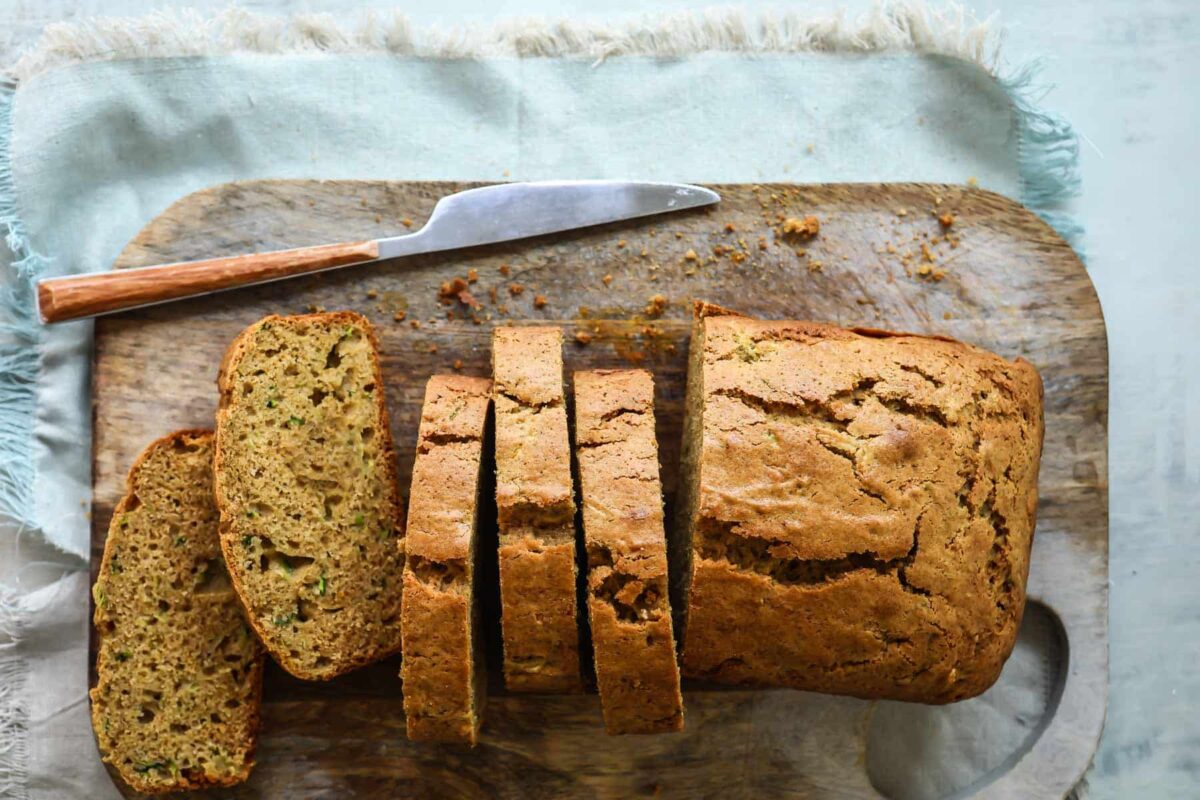 A loaf of zucchini bread partially cut into slices on a wooden cutting board.