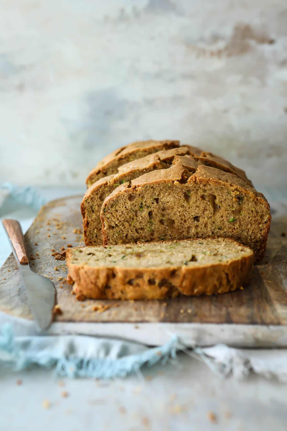 A loaf of zucchini bread cut into slices on a wooden cutting board.