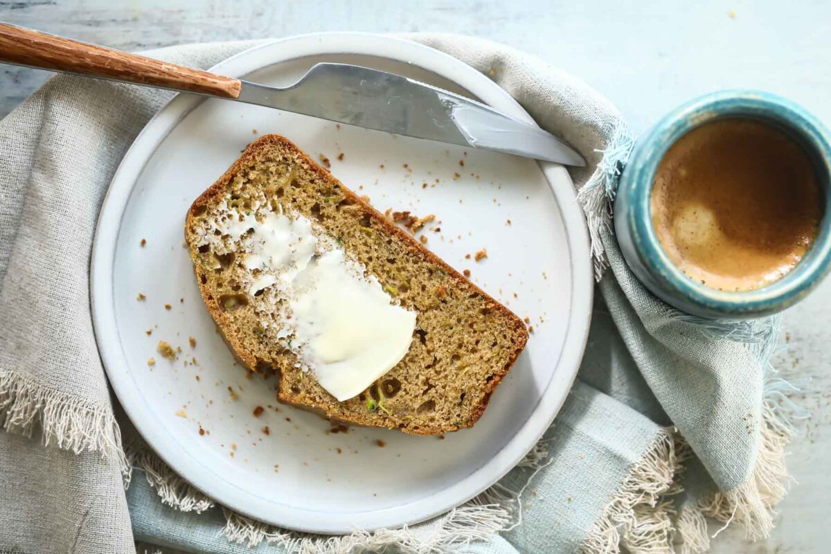 A plate with a slice of zucchini bread with butter spread on it.
