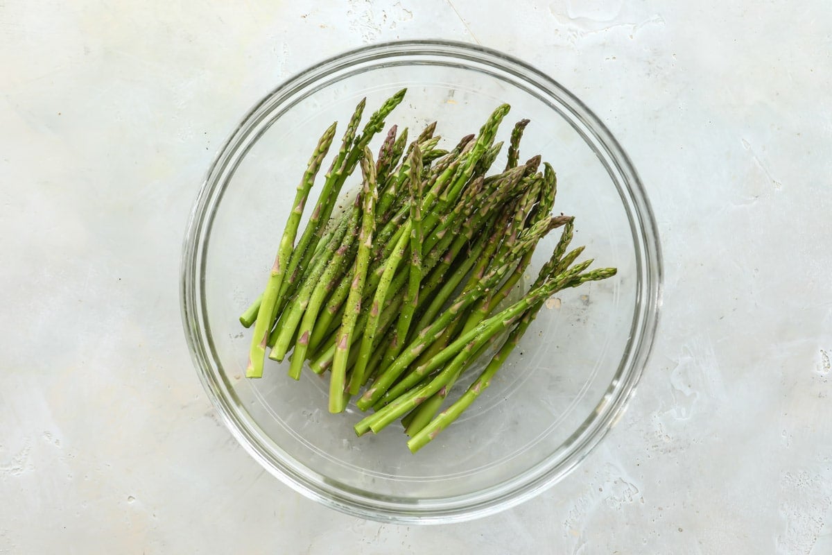 A clear bowl with seasoned raw asparagus in it.