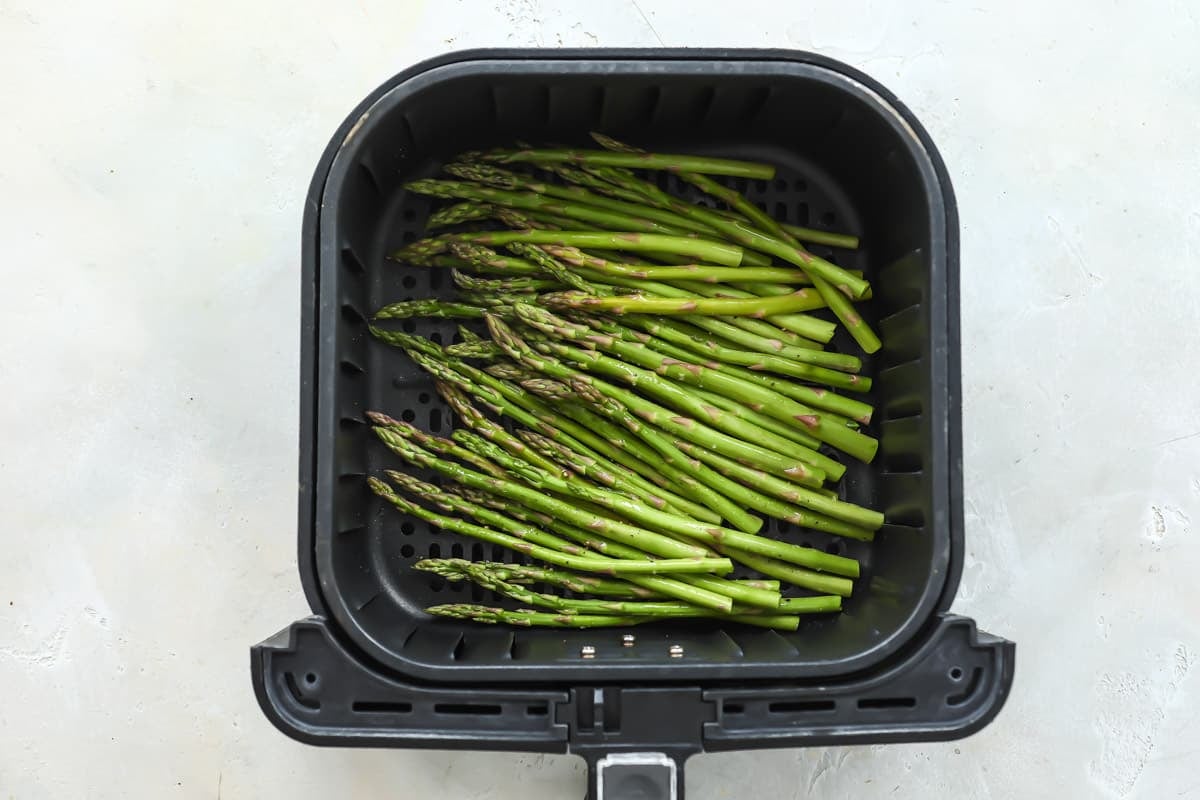 An air fryer basket with raw asparagus in it.