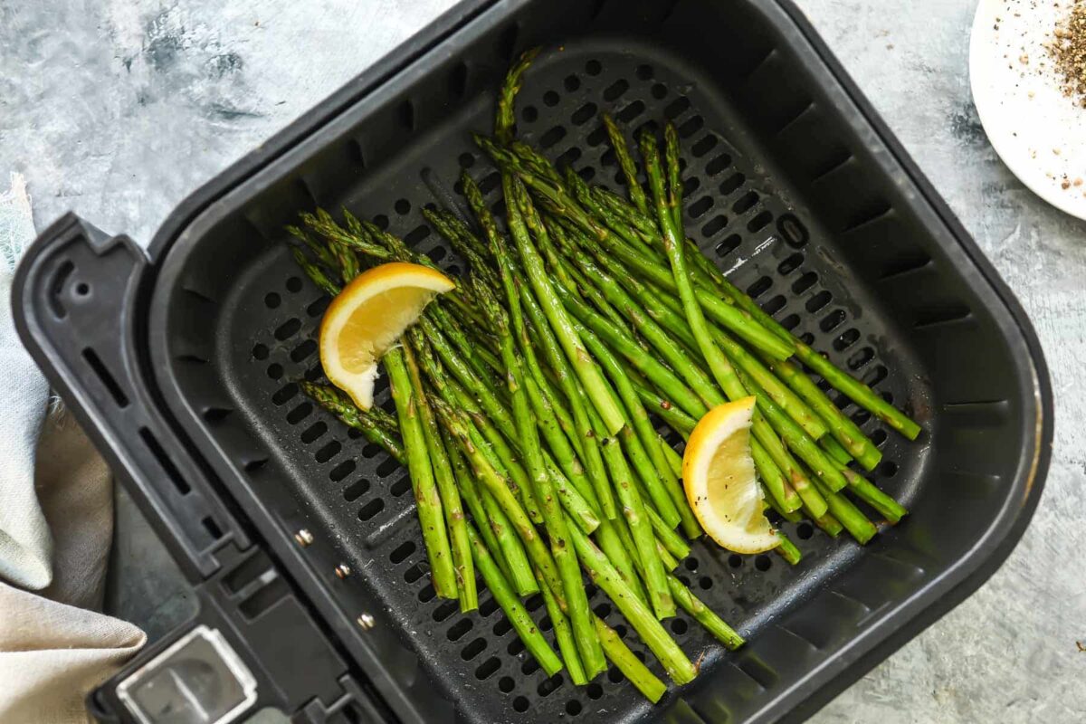 An air fryer basket with asparagus in it.