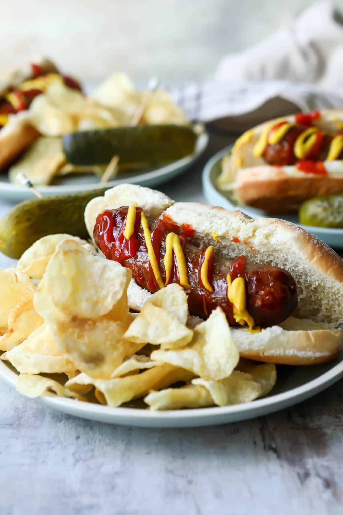 An air fryer bratwurst on a plate with potato chips and a pickle.