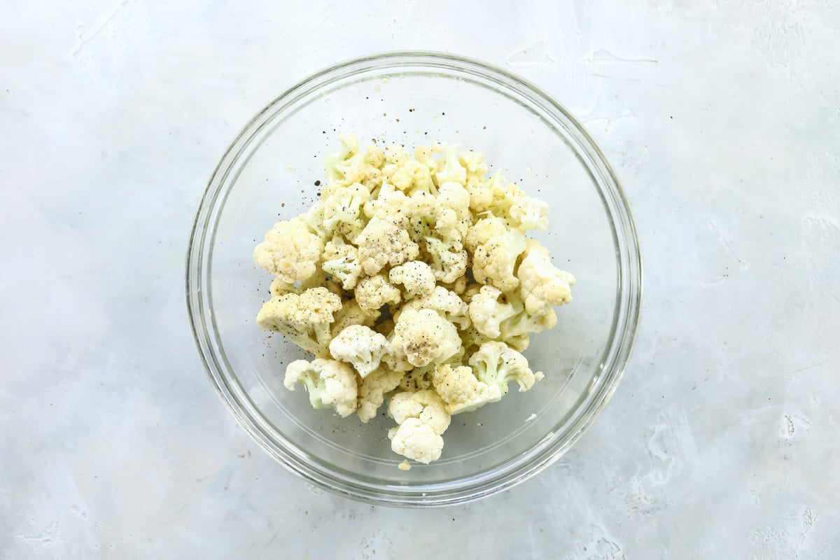 Cauliflower in a glass bowl with olive oil and seasonings.