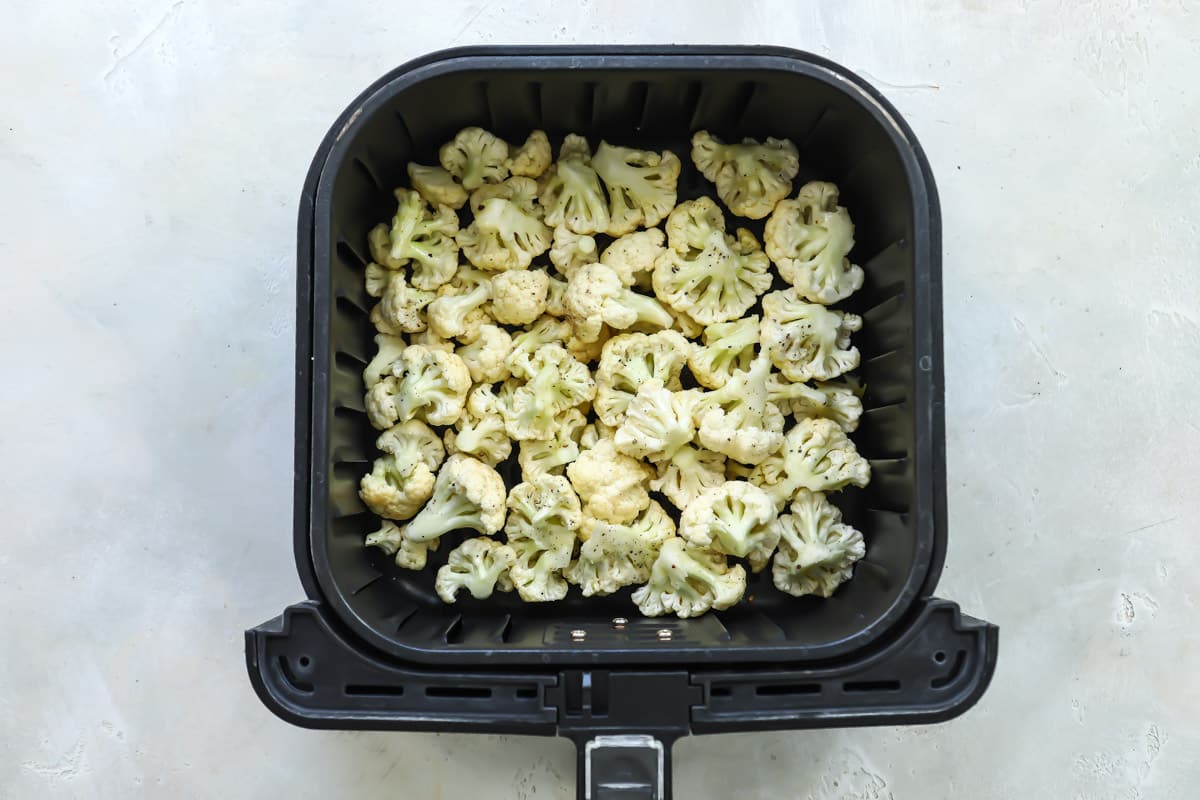 Cauliflower in an air fryer basket before being cooked.