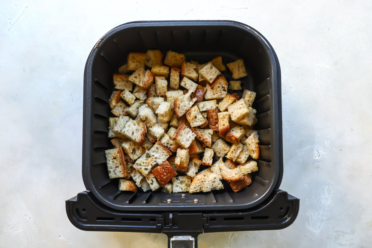 An air fryer basket with bread cubes in it to make croutons.