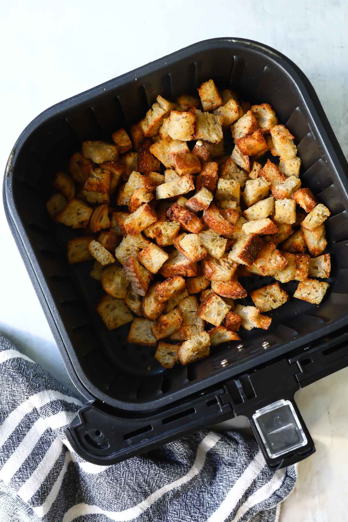 An air fryer basket with croutons in it.