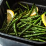 Someone holding an air fryer basket with green beans after being cooked.