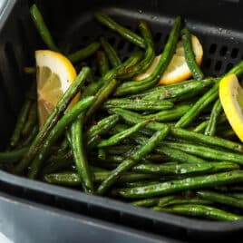 Someone holding an air fryer basket with green beans after being cooked.