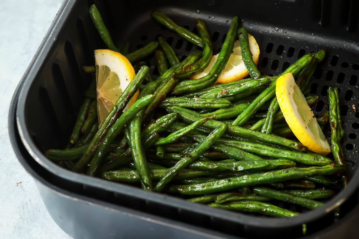 Someone holding an air fryer basket with green beans after being cooked.