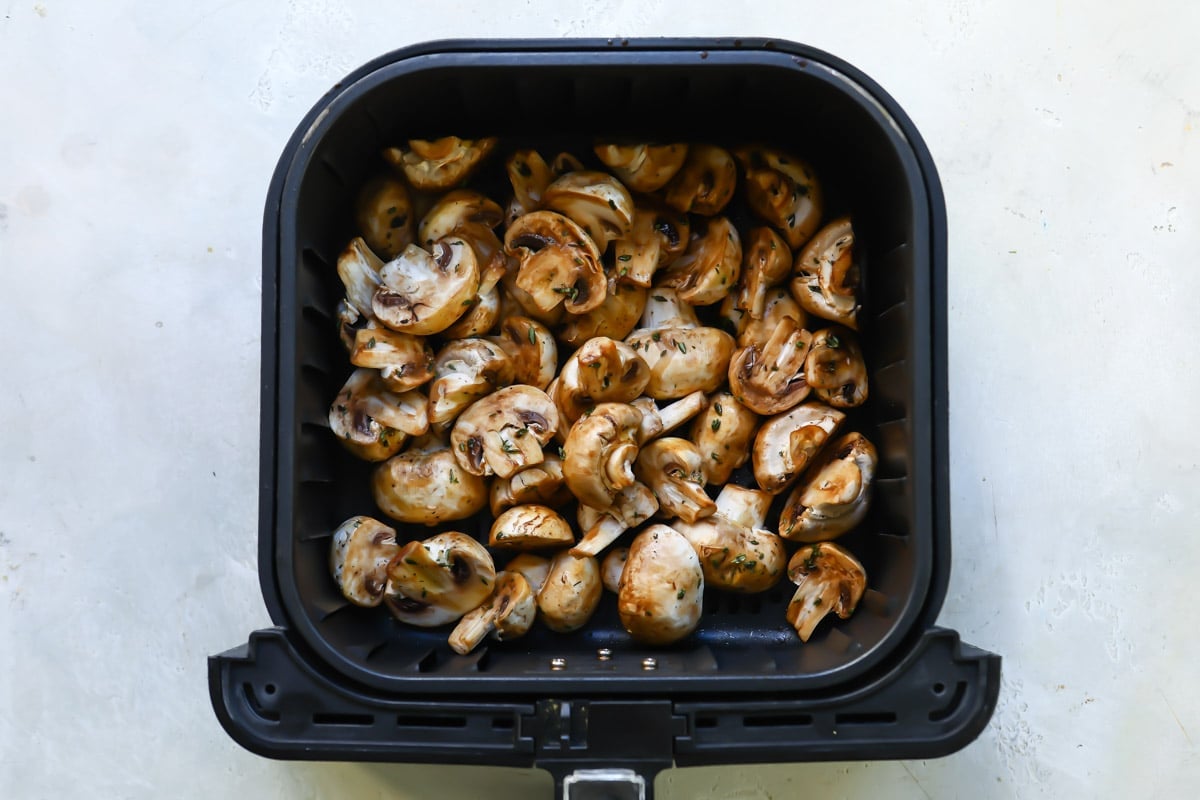 An air fryer basket with mushrooms in it.
