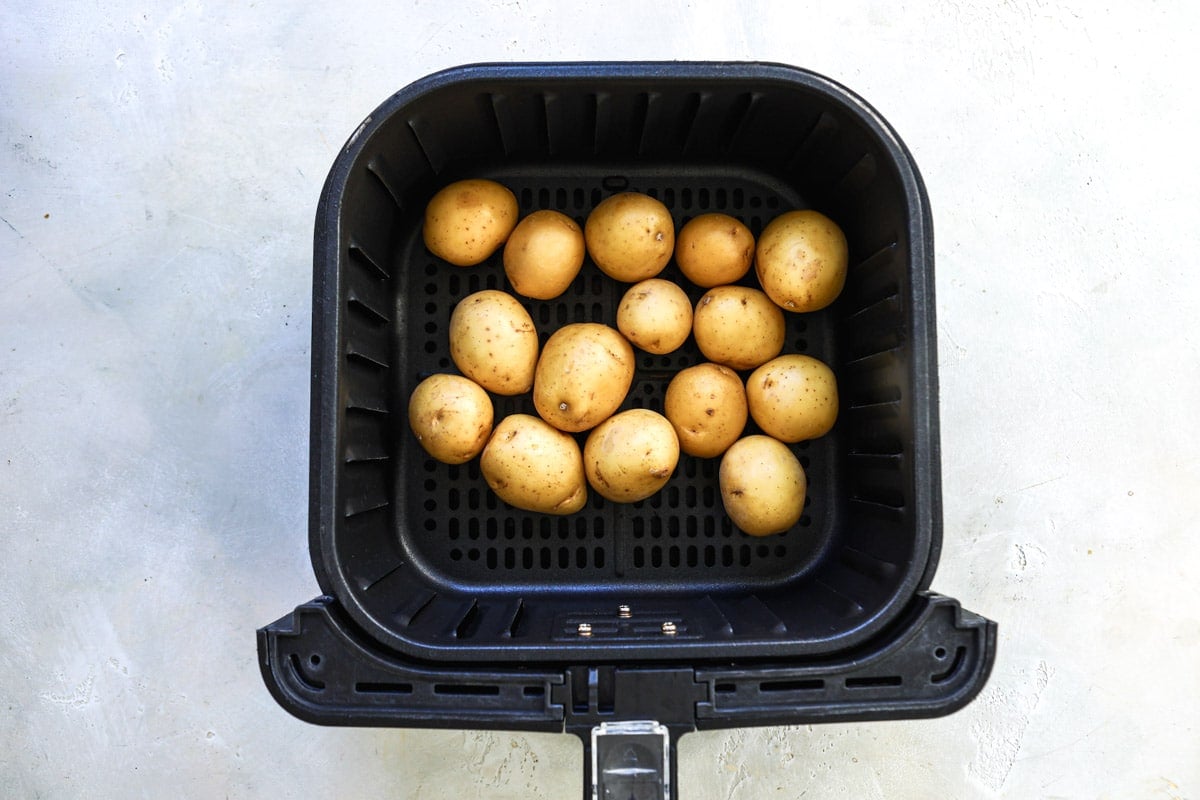 An air fryer basket with baby potatoes in it before being cooked.