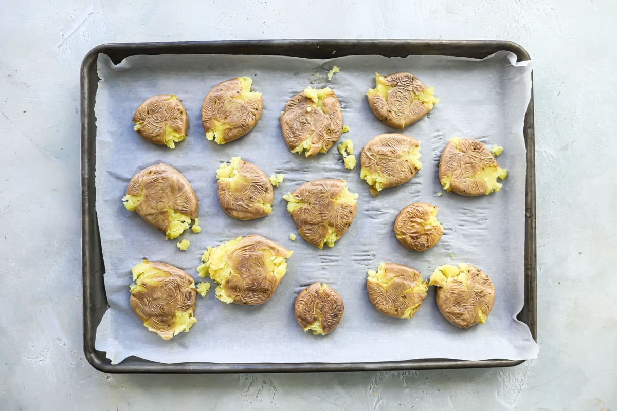 A baking sheet with potatoes that have been smashed.