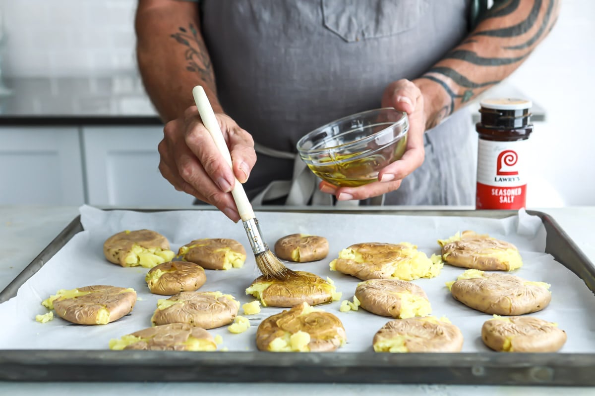 Someone brushing oil on smashed potatoes.