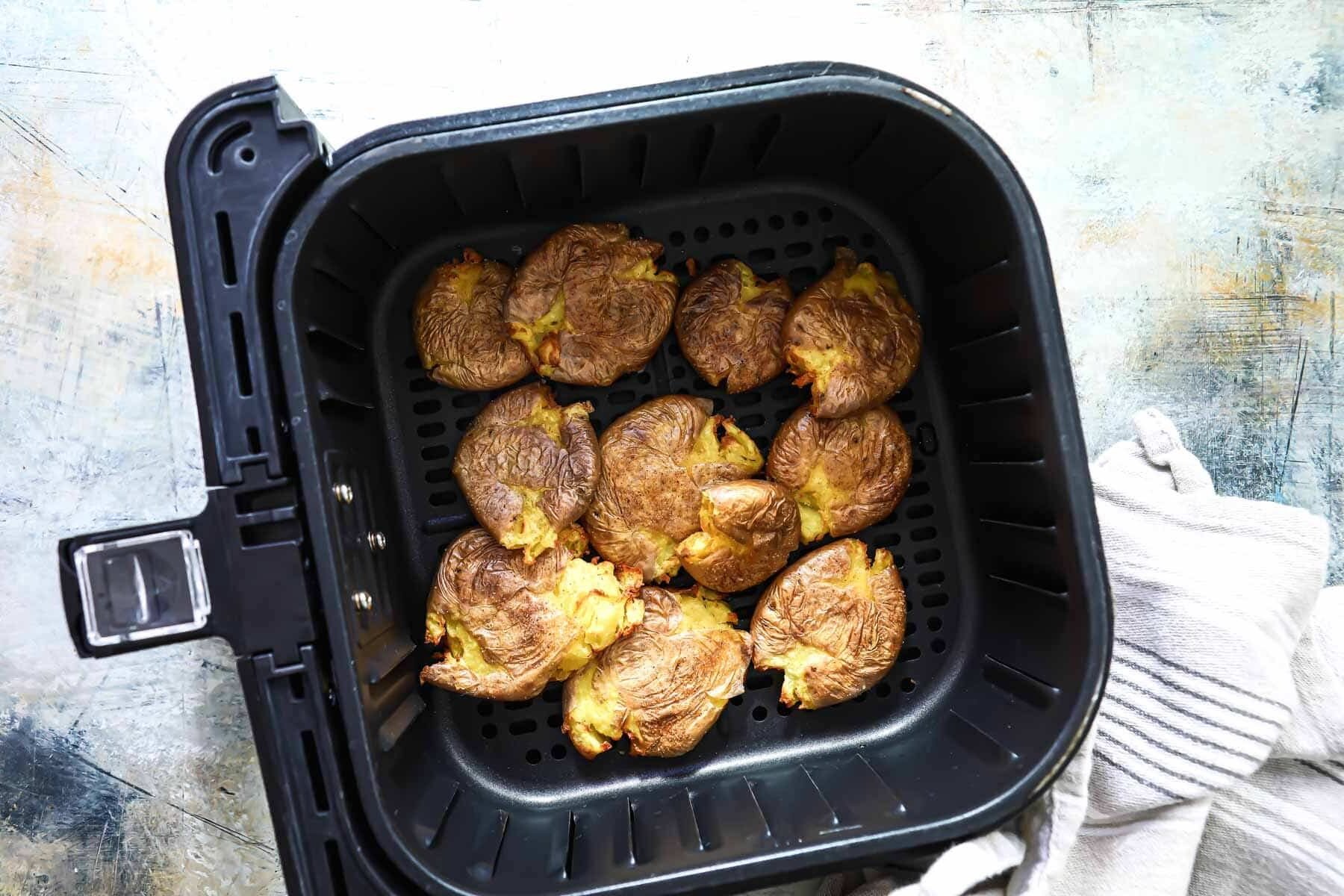 An air fryer basket with smashed potatoes in it.