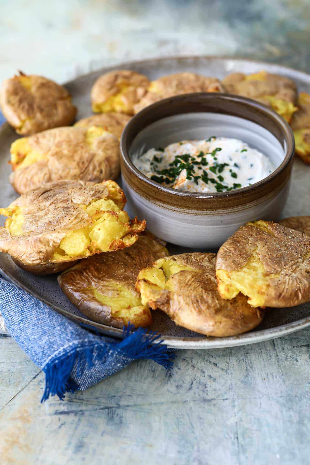 Air fryer smashed potatoes on a platter with a small bowl of white dip in the middle.