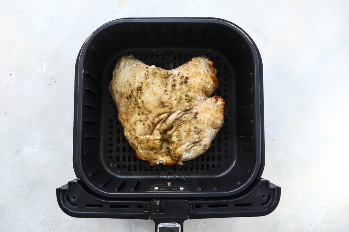 A turkey breast in an air fryer basket before being fully cooked.
