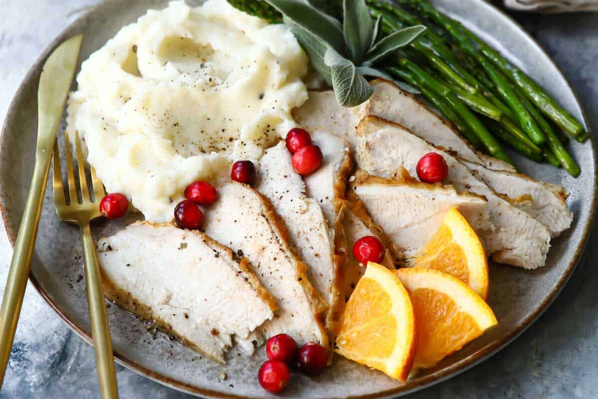 Slices of air fryer turkey on a plate with mashed potatoes and green beans.