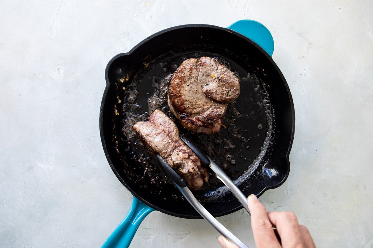 A filet mignon being cooked in a cast iron skillet.