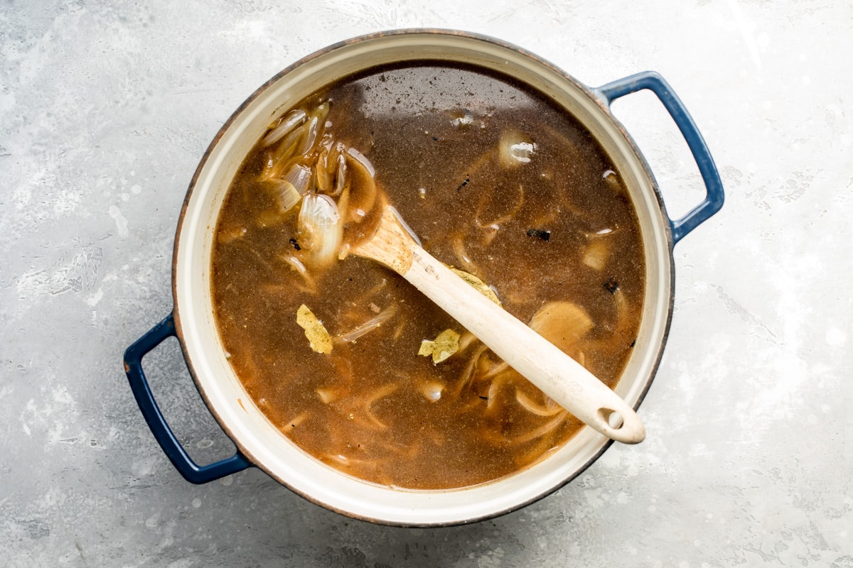 French onion soup ingredients cooking in a blue pot.