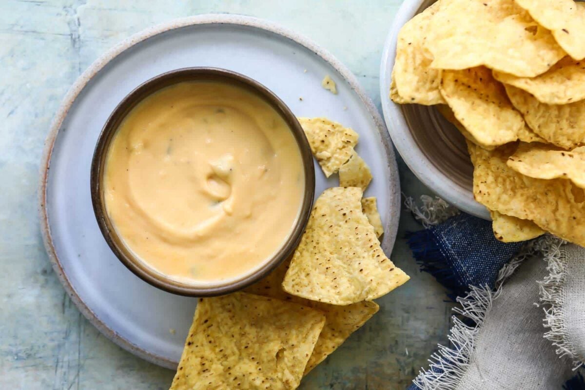 A small bowl of nacho cheese on a plate surrounded by chips.