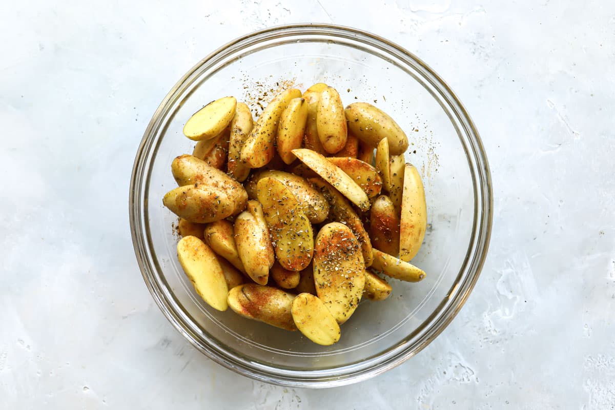 Halved fingerling potatoes in a glass bowl with seasoning.