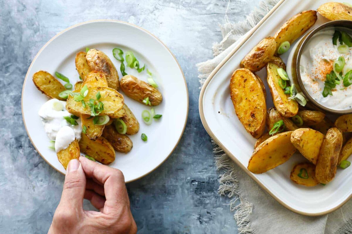 Someone dipping roasted fingerling potatoes in a white dip.