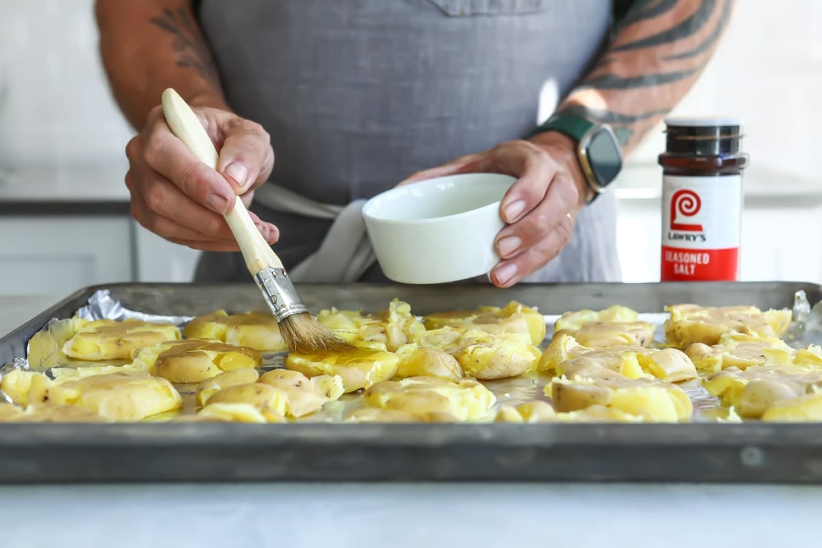 Someone brushing olive oil on smashed potatoes.