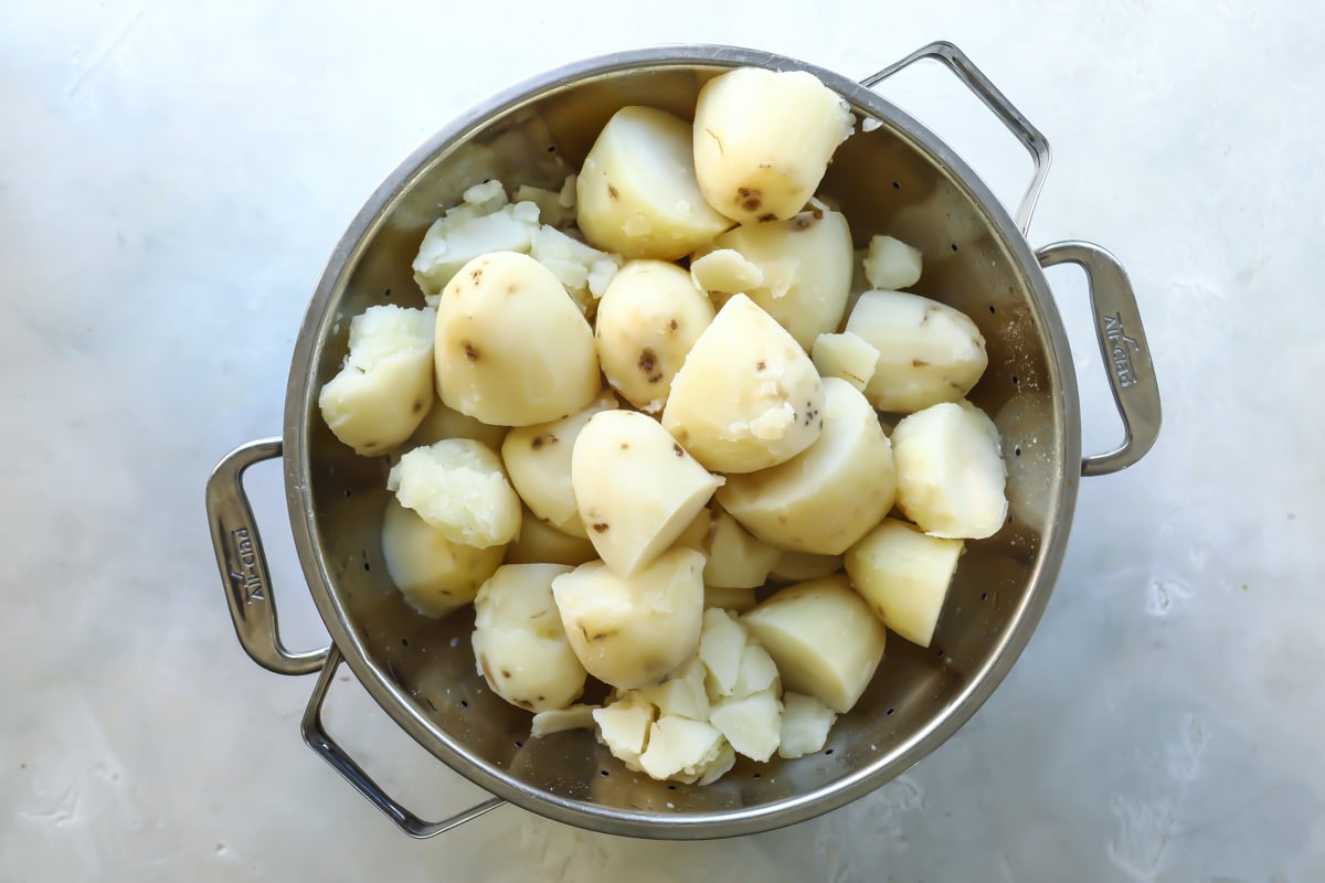 Boiled potato halves in a colander over a stock pot.