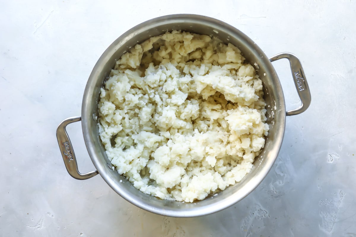 A silver stockpot with paritally mashed potatoes.