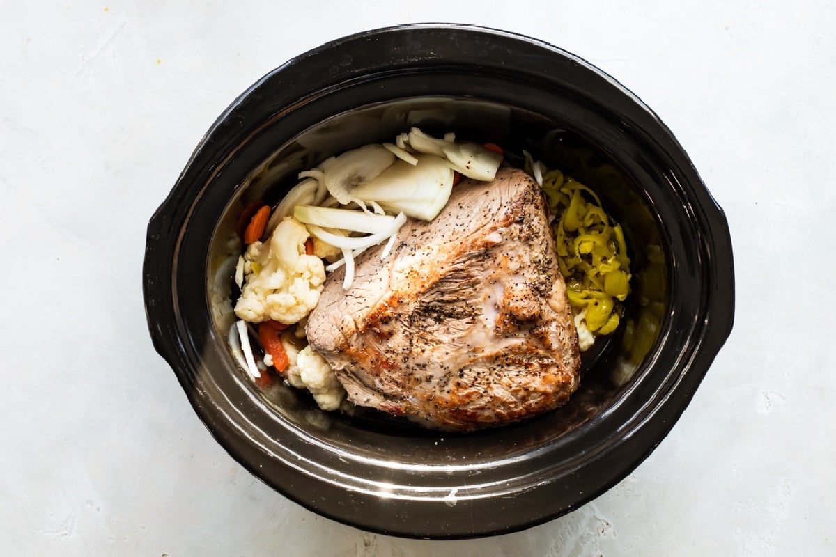 A browned beef roast in a slow cooker with pickled vegetables.