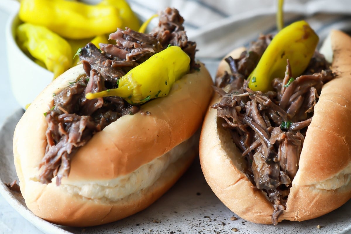 Two Italian beef sandwiches on a plate with pepperoncinis.