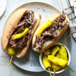 Two Italian beef sandwiches on a plate with pepperoncinis.