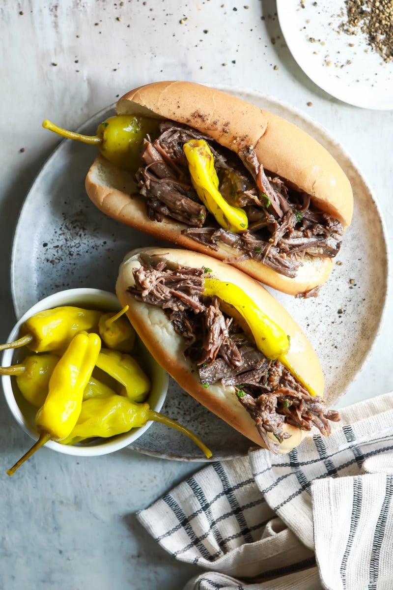 Two Italian beef sandwiches on a plate with pepperoncinis.