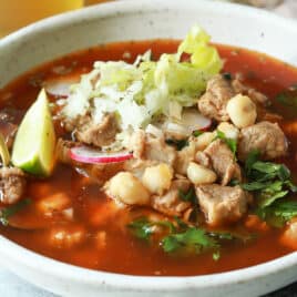 A bowl of pozole rojo next to a bottle of Modelo.