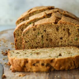 A loaf of zucchini bread partially cut into slices on a wooden cutting board.
