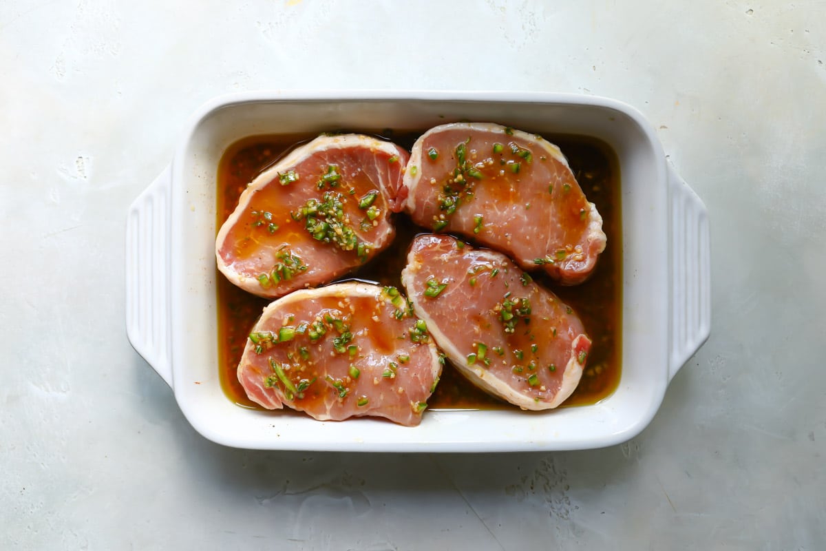 Pork chops marinating in a baking dish.