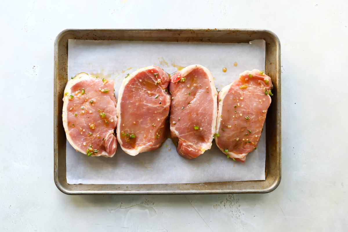 Marinated pork chops on a parchment paper lined baking sheet.