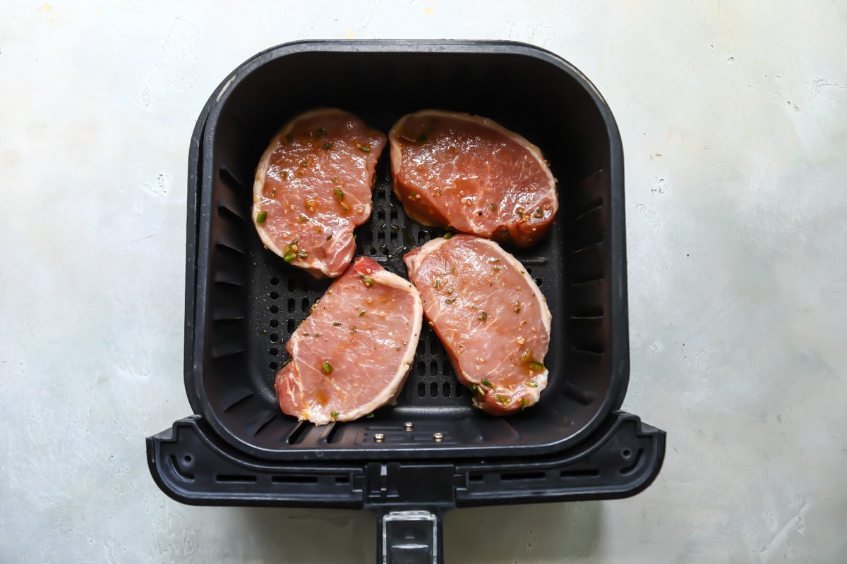 Pork chops in an air fryer before being air fried.